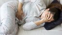 Frau liegt unter Schmerzen auf dem Sofa und hält sich den Bauch.