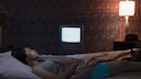 Frau schläft im Bett mit Lampe an, Fernseher an