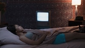 Frau schläft im Bett mit Lampe an, Fernseher an