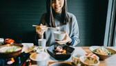 健康的な日本食: 食べ物でいっぱいのテーブルにいる日本人女性