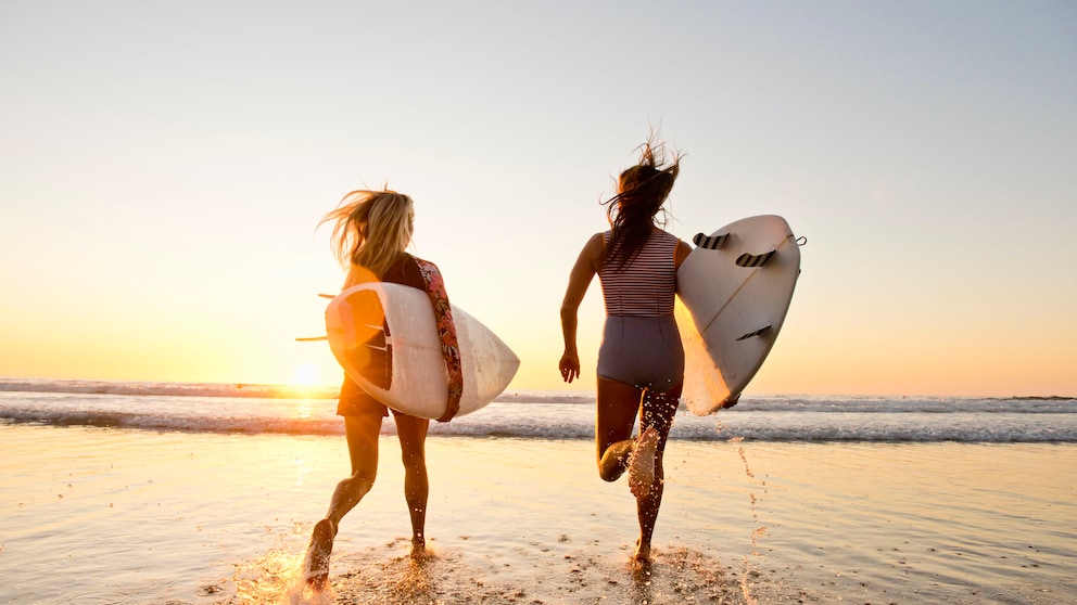 worauf surfer achten: Zwei Frauen mit Surfboards am Strand