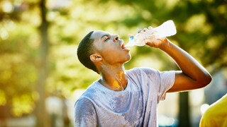 Junger sportlicher Mann trinkt schwitzend Wasser