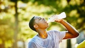 Junger sportlicher Mann trinkt schwitzend Wasser