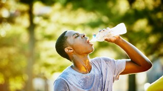 Junger sportlicher Mann trinkt schwitzend Wasser