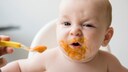 Baby verzieht gesicht, als es mit Brei gefüttert wird