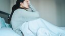 Junge Frau sitzt erschöpft im Bett