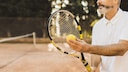 Älterer Mann mit Tennisschläger und und Ball auf dem Platz