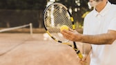 Älterer Mann mit Tennisschläger und und Ball auf dem Platz