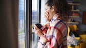 Junge Frau mit Decke umwickelt und tee in der Hand, steht am Fenster.