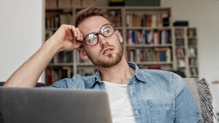 Junger Mann sitzt grübelnd vor dem Laptop