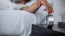 Junger Mann macht im Bett den Wecker aus