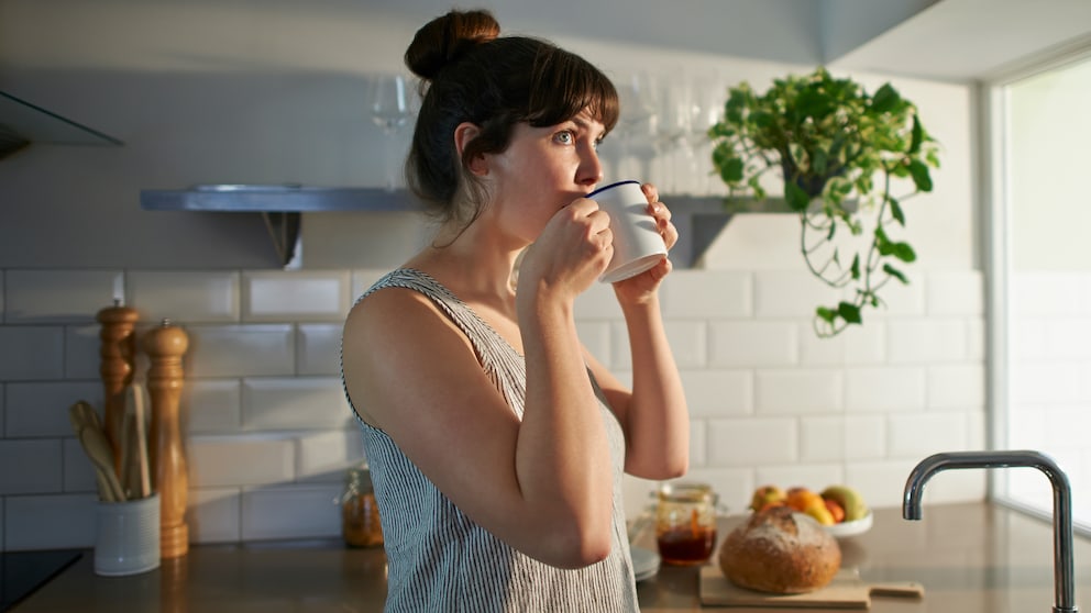 kaffee-abnehmen: Junge Frau steht in der Küche und trinkt Kaffee