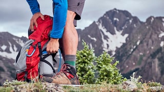 Mann greift in Wanderrucksack zu seinen Füßen