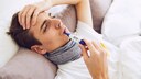 Junger Mann im Bett misst Fieber im Mund