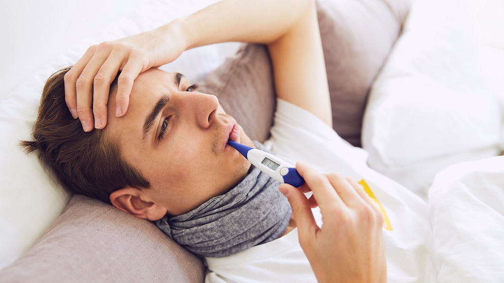 Junger Mann im Bett misst Fieber im Mund