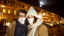 corona szenarien winter: Junges Paar in Winterkleidung, mit Maske und Glühkerzen