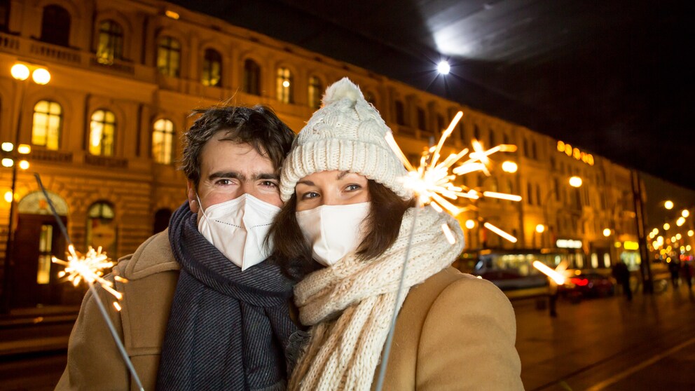 corona szenarien winter: Junges Paar in Winterkleidung, mit Maske und Glühkerzen