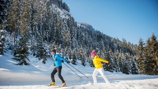 Mann und Frau beim Langlaufen in winterlicher Waldlandschaft