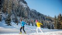Mann und Frau beim Langlaufen in winterlicher Waldlandschaft
