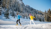 Mann und Frau beim Langlaufen in winterlicher Waldlandschaft