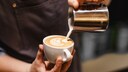Milch im Kaffee gesund: Mann schüttet geschäumte Milch in einen Kaffee