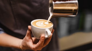 Milch im Kaffee gesund: Mann schüttet geschäumte Milch in einen Kaffee