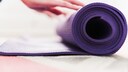 gymnastikmatten yogamatten test: Eine Frau rollt eine Matte zusammen