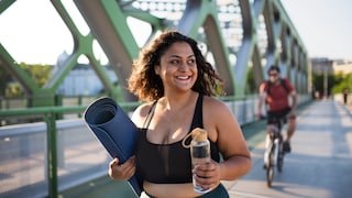 sport übergewicht: Junge kurvige Frau im Sport-Outfit mit Yoga-Matte und Trinkflasche