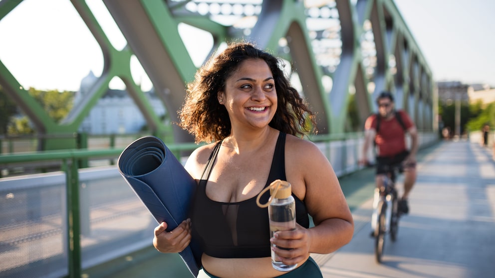 sport übergewicht: Junge kurvige Frau im Sport-Outfit mit Yoga-Matte und Trinkflasche