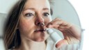 Frau mit Nasenspray im Spiegel