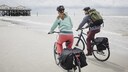 Zwei Personen mit Fahrradzubehör fahrend am Strand