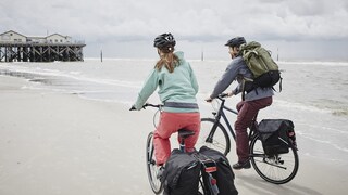 Zwei Personen mit Fahrradzubehör fahrend am Strand