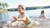 Gefahren beim Baden: Kinder spielen im Wasser am Ufer eines Sees