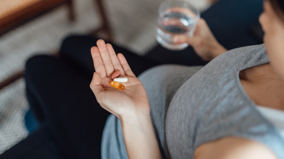 Schwangere hält Vitamintabletten und Glas Wasser in der Hand