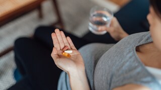 Schwangere hält Vitamintabletten und Glas Wasser in der Hand