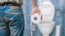 stuhlgang gehirn: Mann mit Klopapierrolle vor einer Toilette