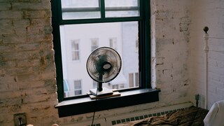 Mann liegt im Bett bei geöffnetem Fenster, Ventilator