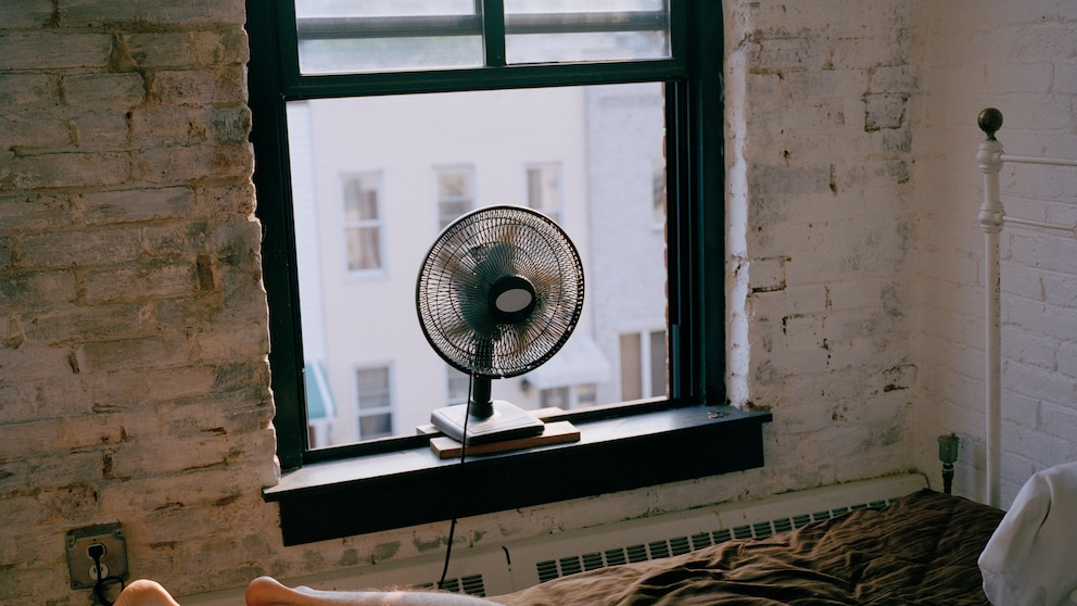 Mann liegt im Bett bei geöffnetem Fenster, Ventilator