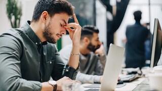 Junger Mann vor Laptop mit Kopfschmerzen