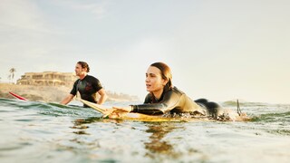 Zwei Personen im Wasser mit Neoprenanzug und Surfboards