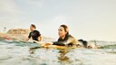 Zwei Personen im Wasser mit Neoprenanzug und Surfboards