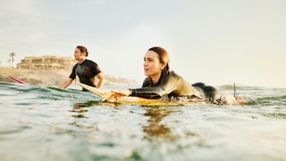 Zwei Personen im Wasser mit Neoprenanzug und Surfboards