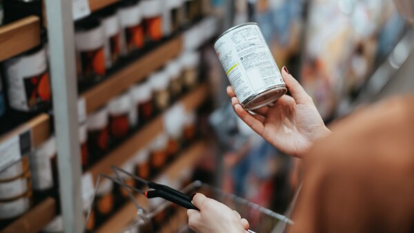 Frau schaut auf Nährwerttabelle einer Dose im Supermarkt