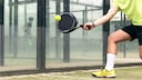 Sportler mit gelbem Shirt und Schuhen spielt Padel.
