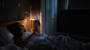 Frau schaut im Bett aufs Handy