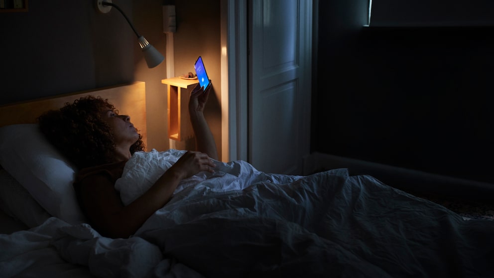 Frau schaut im Bett aufs Handy