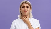 Frau fasst sich mit schmerzverzerrtem Gesicht an den Hals – Mandelentzündung?