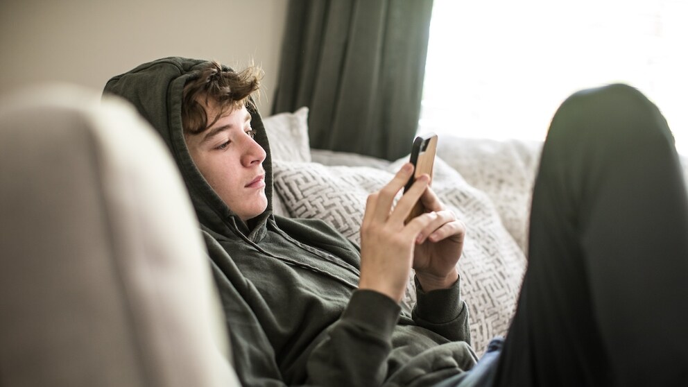 Junge sieht auf sein Handy.