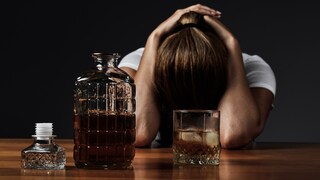 Frau liegt vor einem Glas und einer Flasche Alkohol