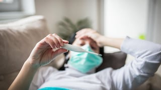 Ill infected woman checking thermometer having fever. Girl wearing protective mask while having cold.